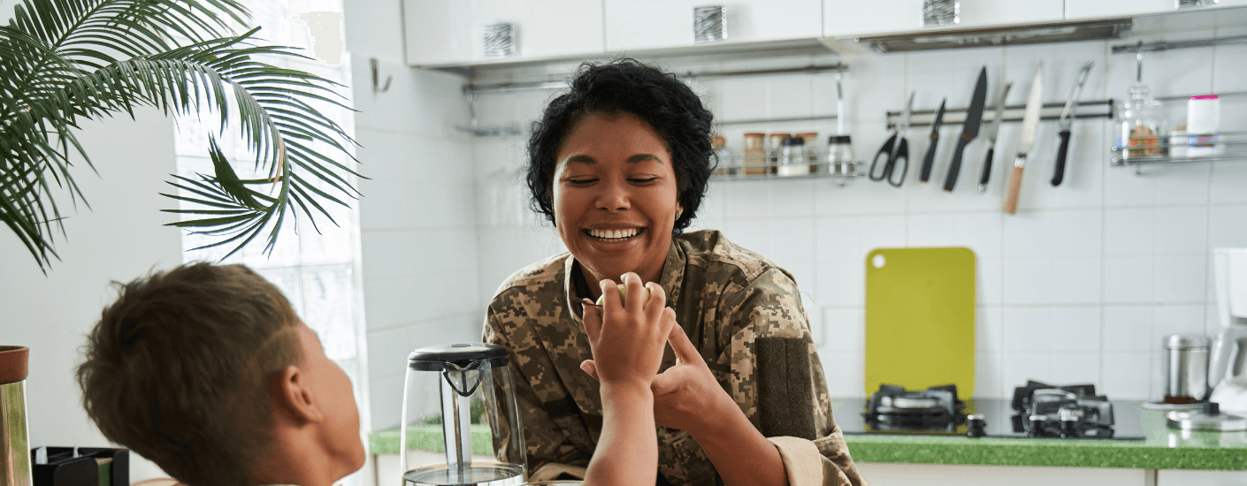 Smiling service member in uniform sharing a moment with a child in a kitchen, accompanying a guide to VA home loans in Guam.
